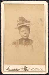 Photograph of a woman wearing a hat and glasses. Printed beneath the image is "Cummings 302 Market St. Wilmington, Del.". The name and address of the photography studio is also printed on the back of the card along with a design of an artist.