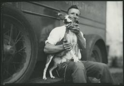 View of man sitting on the running board of a truck with a dog.