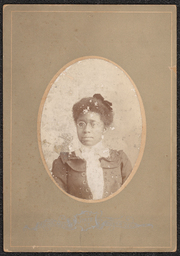 Photograph of a woman placed in a gray-brown board with an oval cut out for the image. The photograph shows the head and shoulders of the woman, and she is wearing glasses. Below the photograph is a metallic stamp with the name and address of the photography studio. It reads: "R.C. Holmes, State Street, Dover, Delaware".
