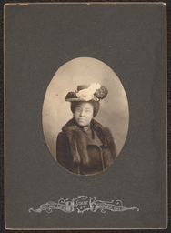 Photograph of a woman in a dark gray frame with an oval cut out. She is wearing a fur coat, hat, and glasses. Beneath the image is a metallic stamp with the name and address of the photography studio: "R.C. Holmes, State St., Wilmington, Del.".