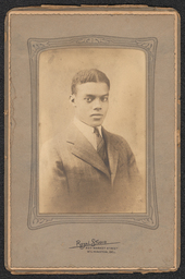 Photograph of a man in a striped suit and tie in a dark gray decorated frame. The name and address of the studio is stamped below the image.
