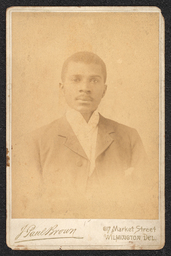 Photograph of a man wearing a suit jacket and white scarf. The portrait is taken from the mid chest up. The name and address of the photography studio is printed along the bottom edge of the cabinet card.