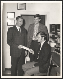 Two men presenting a document to a third, undated