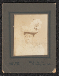 Photograph of a woman wearing a feathered hat, taken from the shoulders up. Mounted on a tan board. Printed under the photograph is "Holland, 311 Market St., Wilmington, Del.".