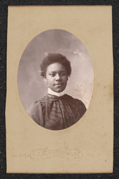 Photograph of a woman wearing a dark dress mounted on a light tan board. Embossed under the photograph is "J.R. Cummings Wilmington, Del.".