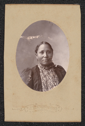 Photograph of a woman wearing a patterned shirt mounted on a light tan board. Embossed underneath the photograph is "J.R. Cummings Wilmington, Del.".