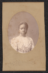 Photograph of a woman wearing a plaid dress mounted on a light tan board. Embossed beneath the photograph is "J.R. Cummings Wilmington, Del.".