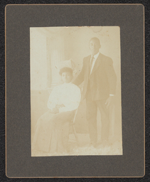 Photograph of a standing man and a seated woman mounted on a black board.