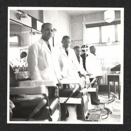 Four barbers pose by their chairs inside of a barbershop