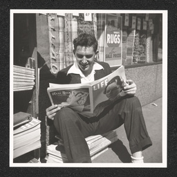 A man reads Life Magazine by a newspaper stand