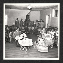 Interior view of Garrett Settlement House at 301 E. 7th St. in Wilmington, Delaware, showing children and teachers. Child second from right with baby carriage is Cynthia Elliot (Oates). During the Depression, settlement houses such as these provided families with food and shelter, and acted as orphanages.