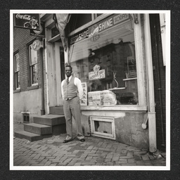 Newspaper Salesman Vernon, man standing outside his shop, March, 1941