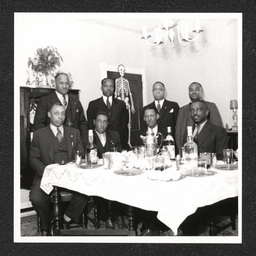 Skeleton Club 510 E. 10th St., eight men at table with skeleton cutout, 1940