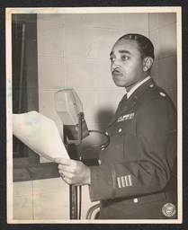 Father Oscar Elliot Holder Poses in Front of a Microphone, undated