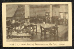 Postcard showing the ballroom at Joe's Black Cat Casino. The room is empty, but there are chairs and tables scattered throughout. In the lower left corner is an inset image of the exterior of the building.