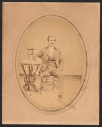 Enlarged photograph of a man with a missing leg and crutches leaned against a small side table next to him. From the studio of Wilmington photographer Emily Webb.