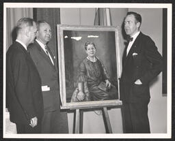 Three men in suits next to easel with portrait of Emily Bissell, undated