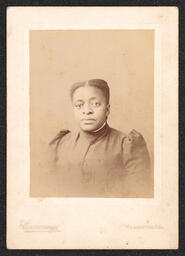Photograph of a woman wearing a dark dress, taken from the shoulders up. The photograph is in a white card frame. Embossed on the bottom edge of the card is "Cummings Wilmington, Del.".