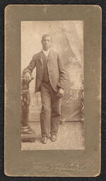 Photograph of a man posing with a small pillar. The photograph is mounted on dark brown card. Very faintly embossed under the photograph is "Wilmington Photo Co., 412 Market St. Wilmington, Del.".