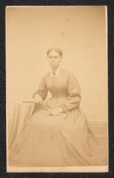Photograph, Seated woman next to a table, front