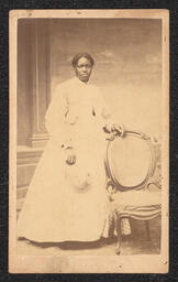 Photograph, Woman wearing a white dress posing with a chair, front