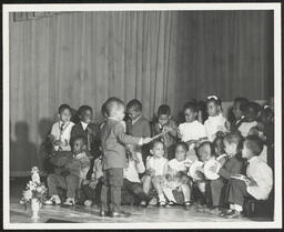 Child conducts group of children with musical instruments on stage, circa 1945-1965
