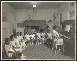 Graduating class sits in semi-circle around teacher at piano, 1947