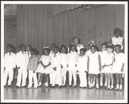Group of children standing in line to perform with two teachers chaperoning.