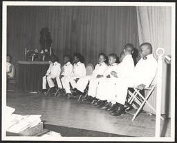Group of boys in white suits sitting on stage at St. Michael's Day Nursery.