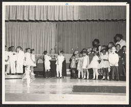 Two children light candles in chapel while other children and teachers look on.